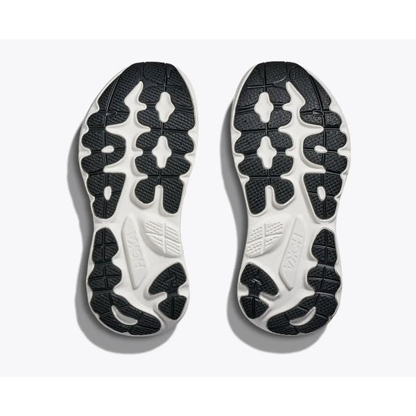 Et par Hoka Gaviota 6 Dame-såler i sort/hvid vises side om side, set nedefra. De har hovedsageligt hvid bund med sorte gummimønstre og HOKA-logoet på venstre sål, alt sammen på en hvid baggrund.