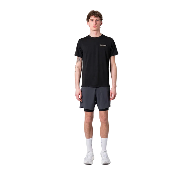 En person står og kigger fremad iført en sort t-shirt, Liiteguard Glu-Tech Running 2In1 Shorts for men in Ebony, hvide strømper og hvide sneakers på en almindelig hvid baggrund.