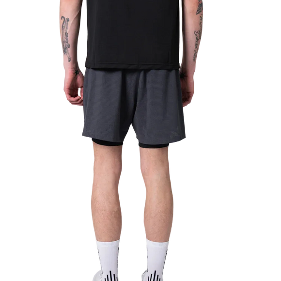 En person vender sig væk fra kameraet iført en sort skjorte og Liiteguard Glu-Tech Running 2In1 Shorts i Ebony. De har synlige tatoveringer på armen, høje hvide sokker og hvide sneakers på en almindelig hvid baggrund.