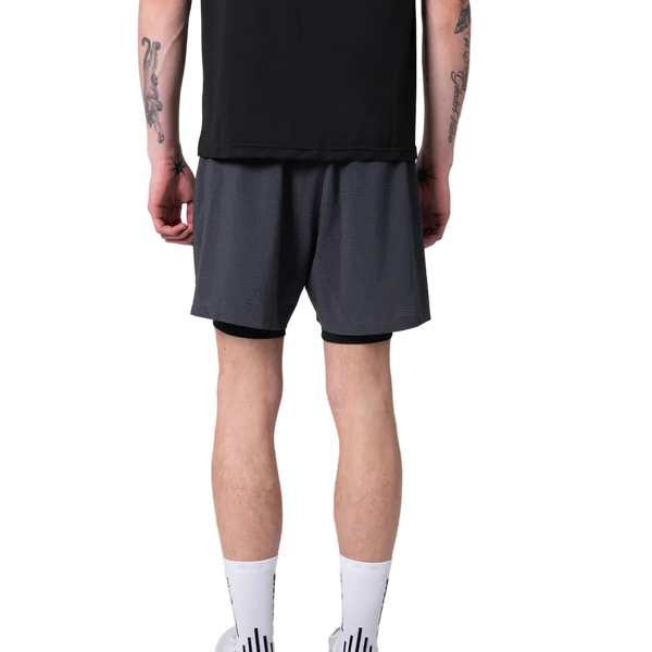En person vender sig væk fra kameraet iført en sort skjorte og Liiteguard Glu-Tech Running 2In1 Shorts i Ebony. De har synlige tatoveringer på armen, høje hvide sokker og hvide sneakers på en almindelig hvid baggrund.