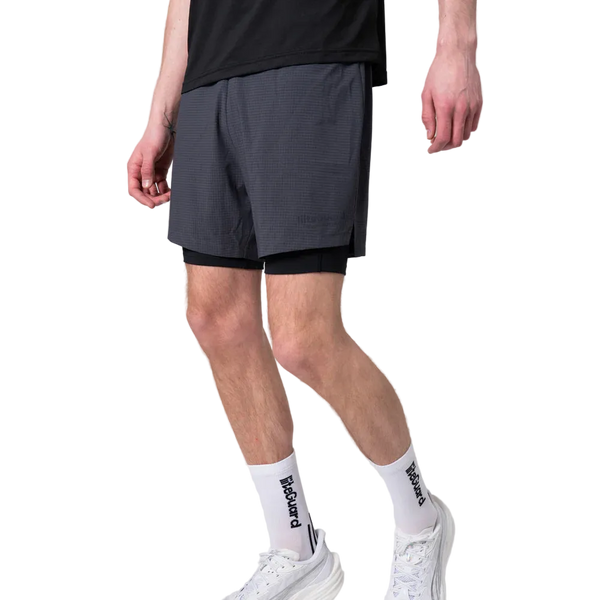 En person er iført en sort T-shirt, Liiteguard Glu-Tech Running 2In1 Shorts Herre Ebony, hvide sokker med sort tekst og hvide sportssko, mens han står mod en almindelig hvid baggrund. Hovedet er ikke synligt på billedet.