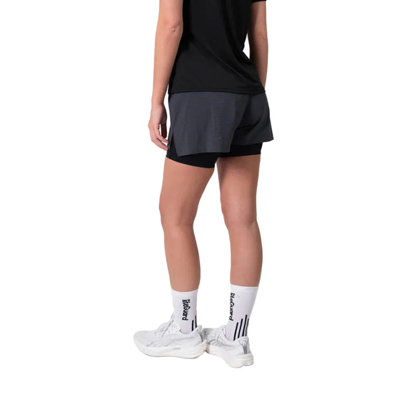 På billedet ses en person set bagfra iført en sort T-shirt, Liiteguard Glu-Tech Running 2-i-1-shorts til kvinder i farven Ebony, hvide strømper med sort tekst og striber samt hvide sneakers, foran en ensfarvet hvid baggrund.