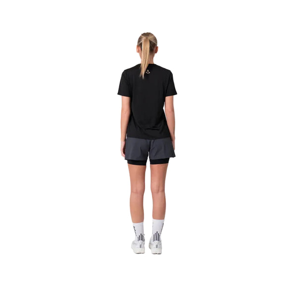 En person med blondt hår i en hestehale står med ryggen til kameraet iført en sort T-shirt, Liiteguard Glu-Tech Running 2-i-1-shorts til kvinder i farven Ebony, hvide sokker og hvide sneakers foran en ensfarvet hvid baggrund.