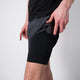 En person iført sorte Liiteguard Glu-Tech Running 2In1 Shorts, Herre, Ebony med en indbygget telefonlomme på siden lægger en smartphone i den; kun underkroppen og hånden er synlige.