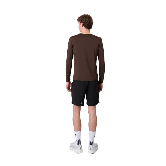 En person står med ryggen til kameraet og har en Liiteguard Ground-Tech Light LS T-shirt, Herre, Coffee Bean på – en brun langærmet løbetrøje til mænd fremstillet af S.Café®-materiale – kombineret med sorte shorts, hvide sokker med et mørkt mønster og hvide sportssko. Baggrunden er ensfarvet og hvid.