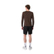 En person står med ryggen til kameraet og har en Liiteguard Ground-Tech Light LS T-shirt, Herre, Coffee Bean på – en brun langærmet løbetrøje til mænd fremstillet af S.Café®-materiale – kombineret med sorte shorts, hvide sokker med et mørkt mønster og hvide sportssko. Baggrunden er ensfarvet og hvid.