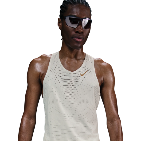 En person med solbriller og Nike M Nk Dfadv Aeroswift Jakob Singlet til mænd i Sail/Metallic Gold står med front mod en almindelig hvid baggrund, hvor huden glitrer, som om den er svedig eller anstrengt.