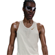 En person med solbriller og Nike M Nk Dfadv Aeroswift Jakob Singlet til mænd i Sail/Metallic Gold står med front mod en almindelig hvid baggrund, hvor huden glitrer, som om den er svedig eller anstrengt.