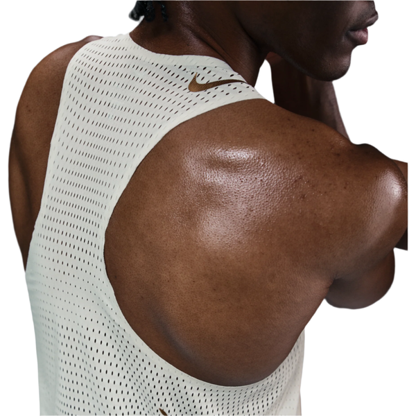 Nærbillede af den øverste del af ryggen og skulderen på en person iført Nike M Nk Dfadv Aeroswift Jakob Singlet til mænd i Sail/Metallic Gold med et lille Nike-logo ved halsen og sved, der afspejler intens træning.