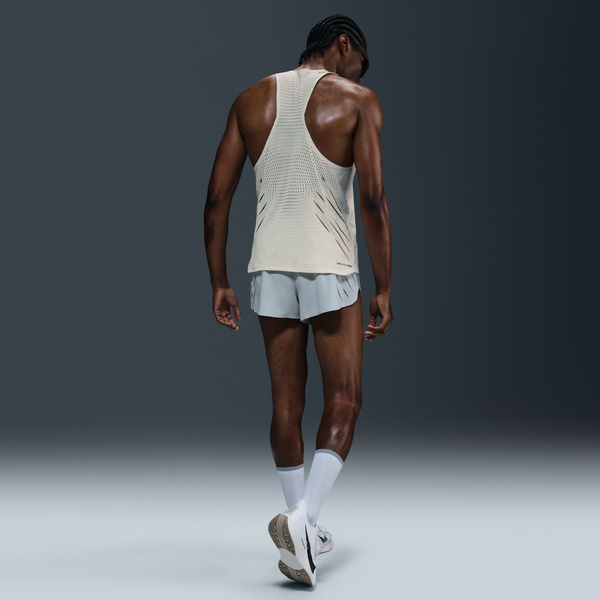 En person er iført Nike M Nk Dfadv Aeroswift Jakob Singlet til mænd i Sail/Metallic Gold sammen med lyse shorts, hvide sokker og løbesko, mens han står på en almindelig mørk baggrund og vender væk fra kameraet.