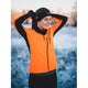 En person i orange jakke og Fusion Headband, Unisex, Black står udendørs i et snedækket landskab, binder håret tilbage og smiler under vintertræningen.