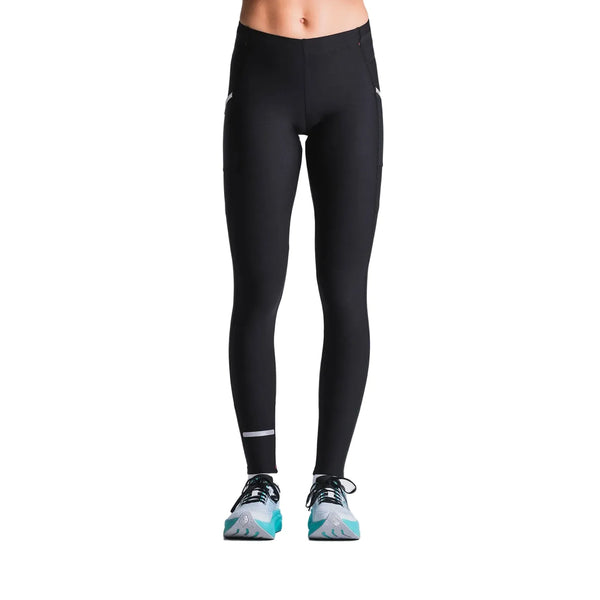 En person, vist fra taljen og ned, er iført Fusion Hot X-Long Tights i sort (unisex) med hvide detaljer og lyseblå løbesko på en almindelig hvid baggrund.