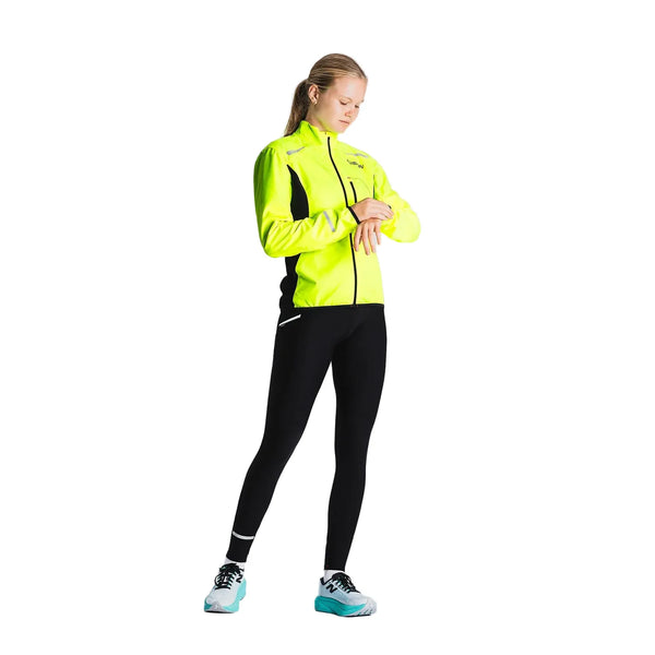 På en almindelig baggrund står en person iført Fusion's Hot X-Long Tights i sort og kigger ned på sit håndled, som om han tjekker et ur eller en fitness-tracker.