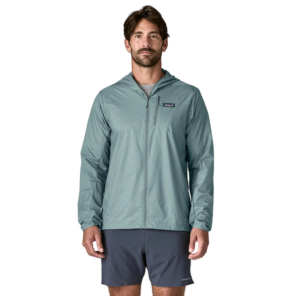 En mand står og kigger fremad iført en Patagonia Houdini Jacket, Herre, i Blue Sage og mørkegrå shorts på en almindelig hvid baggrund.