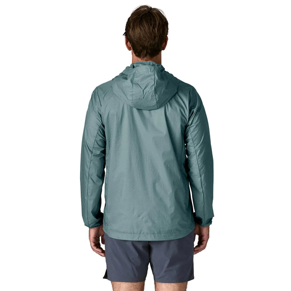 En mand ses bagfra iført en Patagonia Houdini Jacket, Herre, Blue Sage og mørkegrå shorts, stående mod en almindelig hvid baggrund.