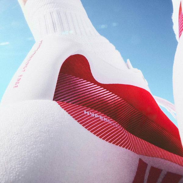 Nærbillede af en person iført Adidas Hyperboost Edge herre løbesko i Cloud White/Pure Ruby/Zero Metalic med Hyperboost Edge-teknologi - stylet med hvide sokker mod en klar blå himmel for komfort og flair.