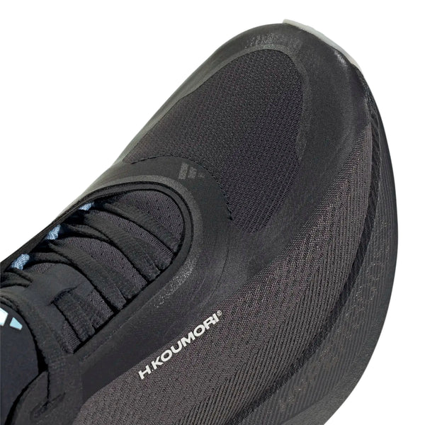 Nærbillede af fronten og siden af en sort sportssko med mesh og syntetiske materialer, snørebånd og mærket Adidas trykt i hvidt på siden tæt på sålen. Denne Hyperboost Edge, Herre, Chacoa/Ntgrey/Alumin x Hermanos Koumori løbesko til herre er designet som en komfortfokuseret model til vejløb og kombinerer støtte med stil til de daglige træningspas.
