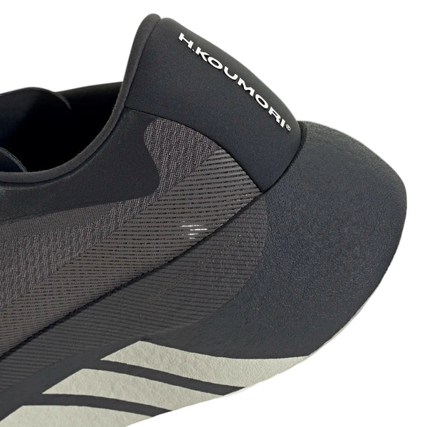 Nærbillede af hælen og siden på den mørke Hyperboost Edge herreløbesko, med Adidas-logoet på bagflappen, geometriske mønstre langs sidepanelet og kontrastfulde, lyse striber på mellemsålen – hvilket fremhæver et komfortfokuseret design til landevejsløb i samarbejde med Hermanos Koumori.
