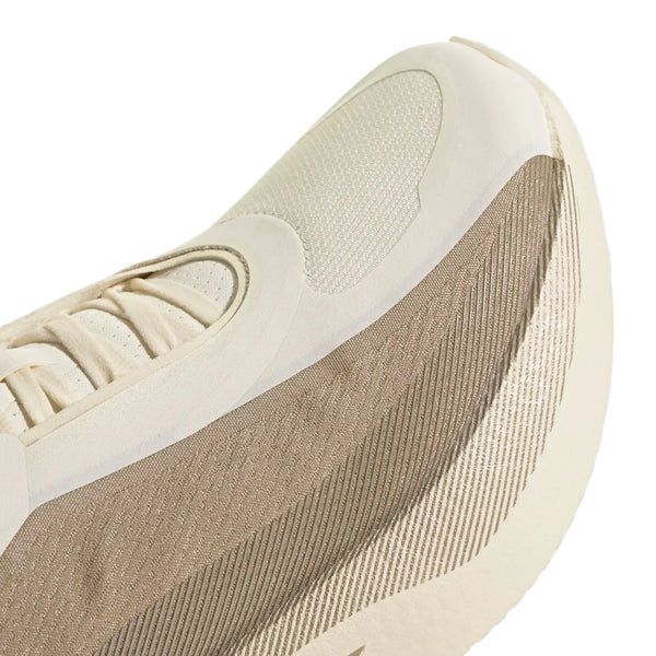 Nærbillede af en beige og cremefarvet sportssko, såsom Adidas Hyperboost Edge til mænd i farvekombinationen Off White/Wonder Cargo, hvor der lægges vægt på den strukturerede overdel i stof, snørebåndene og et udsnit af den tykke, mønstrede sål. Designet fremhæver glatte materialer og mesh i neutrale nuancer fra Adidas, der sikrer optimal komfort ved løb på vej.