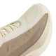 Nærbillede af en beige og cremefarvet sportssko, såsom Adidas Hyperboost Edge til mænd i farvekombinationen Off White/Wonder Cargo, hvor der lægges vægt på den strukturerede overdel i stof, snørebåndene og et udsnit af den tykke, mønstrede sål. Designet fremhæver glatte materialer og mesh i neutrale nuancer fra Adidas, der sikrer optimal komfort ved løb på vej.