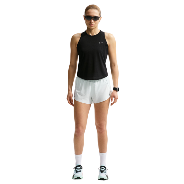 En person ser fremad iført solbriller, en sort Nk Swift Nvlt Brthe Tank fra Nike (Dame, Black/Black/White/Reflective Silv), hvide sportsshorts, sokker og løbesko samt et smartwatch på venstre håndled. Baggrunden er helt hvid.