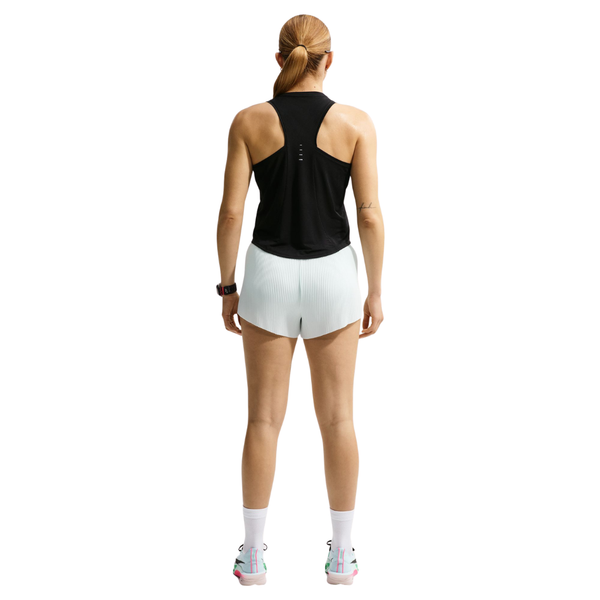 En person med langt tilbagestrøget hår står med ryggen til og er iført en sort Nike Nk Swift Nvlt Brthe Tank Dame, hvide sportsshorts, hvide sokker og hvide løbesko med lyserøde detaljer på en hvid baggrund.