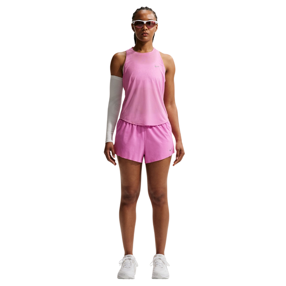 En person står med ansigtet fremad iført en Nike Nk Swift Nvlt Brthe Tank til kvinder i Lt Magenta/Photon Dust/Reflective Silv, matchende pink shorts, hvide sneakers, et hvidt ærme på venstre arm og solbriller. Baggrunden er hvid.