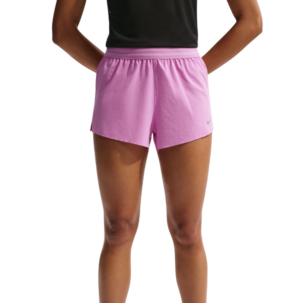 En person står med hænderne på hofterne iført en sort skjorte og Nike Swift Breathe Mid-Rise 2.5" løbeshorts til kvinder i Lt Magenta/Photon Dust/Reflective Silver. Baggrunden er helt hvid.