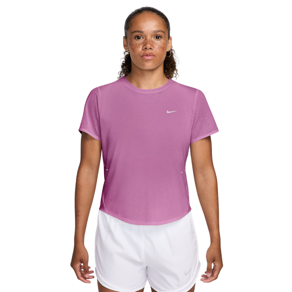 En kvinde står med ansigtet fremad i en lys magenta Nike Nk Swft Nvlt Brthe Ss Top (Dame, Lt Magenta/Photon Dust/Reflective Silv) og hvide Nike-atletikshorts mod en almindelig hvid baggrund.