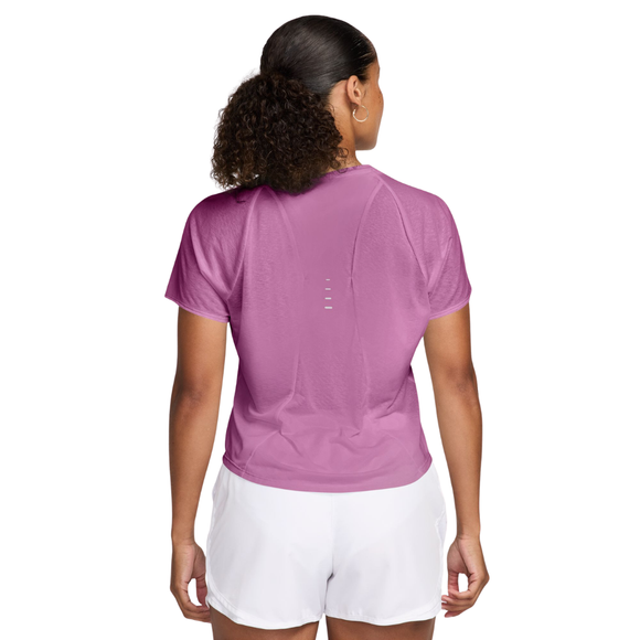 En person med krøllet hår i en hestehale står med ryggen til kameraet iført en Nike Nk Swft Nvlt Brthe Ss Top til kvinder i Lt Magenta/Photon Dust/Reflective Silv og hvide shorts.