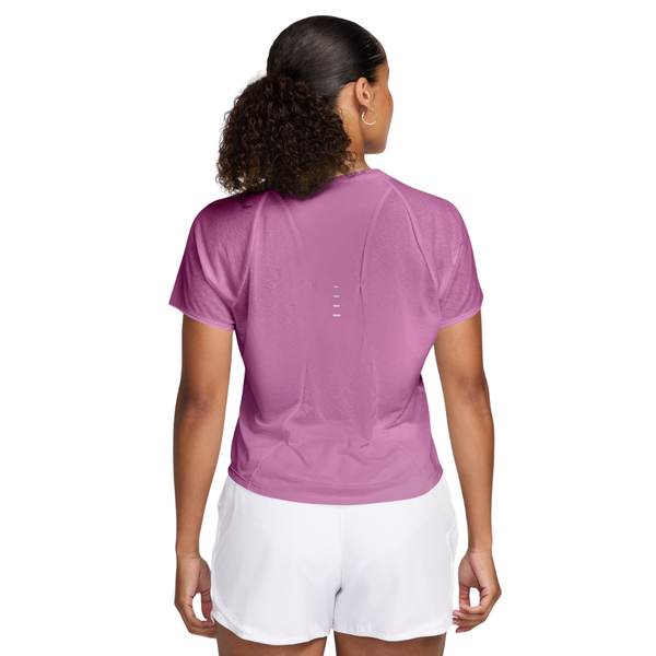 En person med krøllet hår i en hestehale står med ryggen til kameraet iført en Nike Nk Swft Nvlt Brthe Ss Top til kvinder i Lt Magenta/Photon Dust/Reflective Silv og hvide shorts.