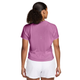 En person med krøllet hår i en hestehale står med ryggen til kameraet iført en Nike Nk Swft Nvlt Brthe Ss Top til kvinder i Lt Magenta/Photon Dust/Reflective Silv og hvide shorts.