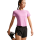 En kvinde i en pink Nk Swft Nvlt Brthe Ss Top, Dame by Nike og sorte shorts strækker benet og holder sig kølig i denne Dri-FIT løbe-T-shirt mod en almindelig hvid baggrund.