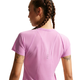 En kvinde med flettet hår ses bagfra iført en kortærmet Nike Nk Swft Nvlt Brthe SS Top i Lt Magenta/Photon Dust/Reflective Silv med syningsdetaljer og reflekterende detaljer på den øverste del af ryggen.