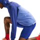 En mand i blå jakke med hætte, shorts, røde sokker, orange sportssko og Nike Stride Running Half Tights (Herre, Lapis/Reflective Silv) ses knælende i et udfald fra siden mod en hvid baggrund.