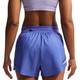 En kvinde iført en lyslilla sports-bh og Nike Nk Arswft Dfadv 3In Short Gx, Dame, Sapphire/Hot Lava kigger væk og viser ryggen med en elastisk linning, en lille lynlåslomme bagpå og Dri-FIT ADV-teknologi for komfort.