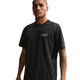En mand ser frem for sig i en sort Nike ACG Dri-FIT T-shirt, Herre, med All Conditions Gear-tekst og lille logo på venstre bryst. Den fugttransporterende skjorte passer til udendørs aktiviteter; hans arme har tatoveringer, og hans udtryk er neutralt.