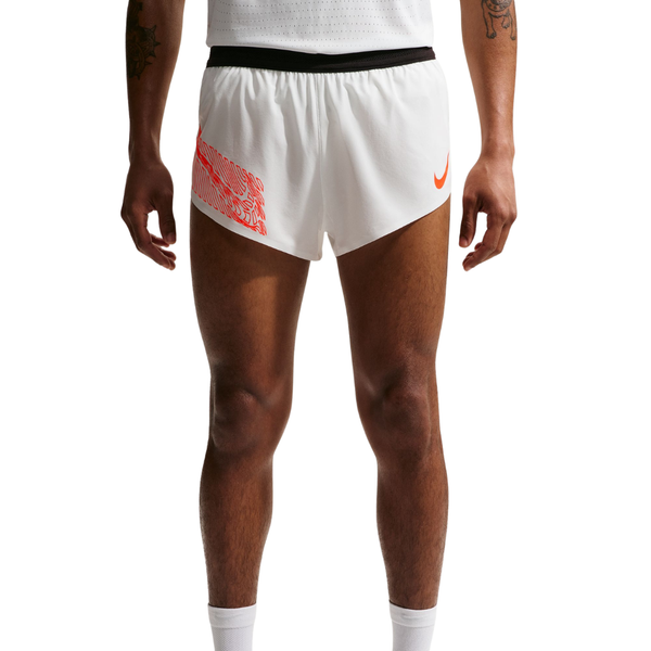 En person er iført Nike Nk Dfadv Arswft Gfx 2Bf Shrt herre i Summit White med et orange Nike-logo på venstre ben, en rød grafik på højre og Dri-FIT ADV-teknologi. Den hvide trøje og sokkerne er synlige; billedet er beskåret ved brystet og under knæene.