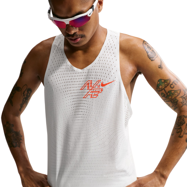 En person iført hvide solbriller og Nike Nk Dfadv Aeroswift Gfx Snglt, Herre, i farven Summit White med røde grafiske detaljer og det ikoniske Nike-logo kigger nedad. Denne luftige, perforerede tanktop er udstyret med Dri-FIT ADV-teknologi, der sikrer optimal komfort under løbetræning. Personens arme er tatoverede og fremstår tydeligt mod en ensfarvet hvid baggrund.
