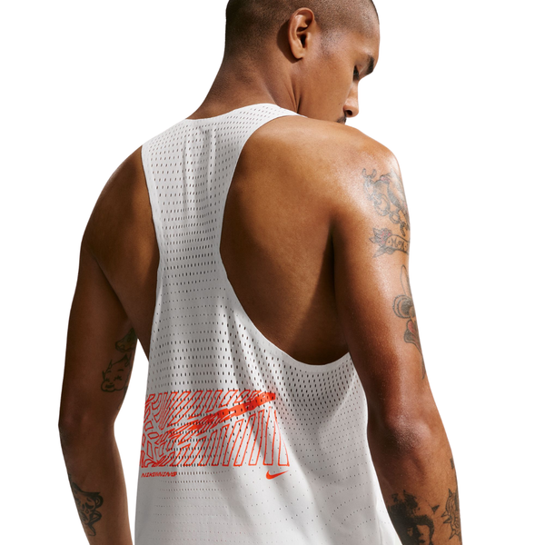 En person med kort hår og tatoveringer på armene ses bagfra, iført Nike Nk Dfadv Aeroswift Gfx Snglt til mænd i farven Summit White. Denne singlet er designet med Dri-FIT ADV-teknologi for optimal komfort under løbetræning og har et rødt grafisk motiv samt et lille Nike-logo nederst på ryggen, hvilket gør det muligt at se detaljer af huden og tatoveringerne gennem det hvide, perforerede materiale.