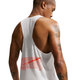 En person med kort hår og tatoveringer på armene ses bagfra, iført Nike Nk Dfadv Aeroswift Gfx Snglt til mænd i farven Summit White. Denne singlet er designet med Dri-FIT ADV-teknologi for optimal komfort under løbetræning og har et rødt grafisk motiv samt et lille Nike-logo nederst på ryggen, hvilket gør det muligt at se detaljer af huden og tatoveringerne gennem det hvide, perforerede materiale.