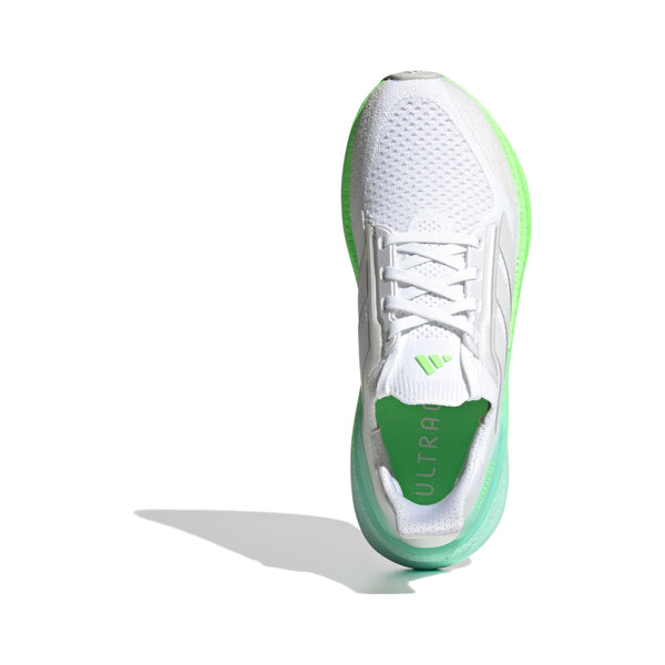 En hvid Adidas Ultraboost 5X Dame løbesko med grønne detaljer og overdel i mesh er vist ovenfra på en hvid baggrund, der kaster en skygge til venstre. På indersålen står der ULTRA, hvilket antyder Boost-teknologiens komfort og ydeevne.