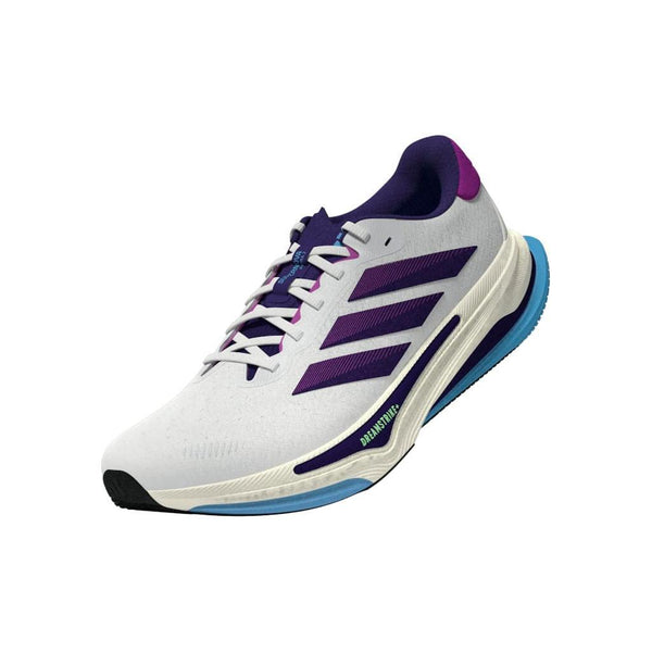 Adidas Supernova Prima 2 Dame løbesko i Cwhite/Cpurpl/Seblbu har en hvid base, lilla striber og accenter, blå ydersål og neongrønne detaljer nær sålen, designet til stabilt løb, vist i en vinkel på en hvid baggrund.