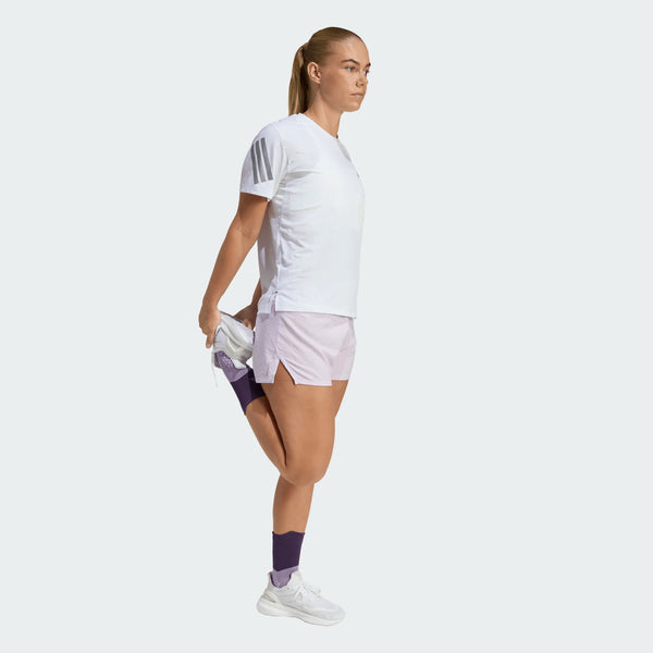 Iført en Adidas Adi365 Running Tee, Dame, White, strækker en person sig ved at holde sin højre ankel bag sig på et ben mod en ensfarvet baggrund - ideelt til løbetræning med adidas Climacool-komfort.