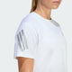 En person iført Adidas Adi365 Running Tee, Dame, i hvid. Man kan se overkroppen og en del af ansigtet; trøjen har tre lysegrå striber på venstre ærme.