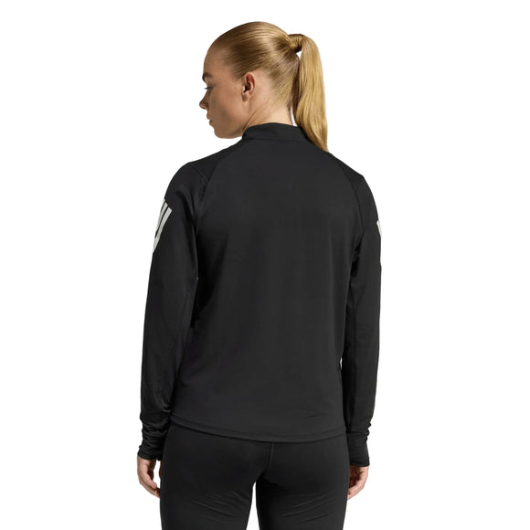 En kvinde med langt blondt hår i hestehale ses bagfra iført Adidas Adi365 Running Iconic Half Zip, Dame, Black, med sorte leggings på en almindelig lysegrå baggrund.
