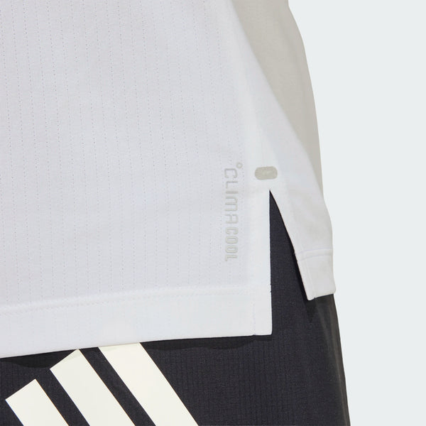 Nærbillede af sidesømmen på en Adidas Adi365 Running Tee, Herre, White, sammen med mørke bukser med kraftige hvide diagonale striber. Baggrunden er ensfarvet og lys.
