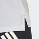 Nærbillede af sidesømmen på en Adidas Adi365 Running Tee, Herre, White, sammen med mørke bukser med kraftige hvide diagonale striber. Baggrunden er ensfarvet og lys.