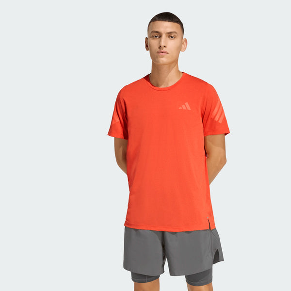 En person kigger fremad iført Adidas Adi365 Running Tee, Herre, Duor - en lys orange løbetrøje med et lille logo på brystet og grå shorts. Hænderne er bag ryggen mod en almindelig lysegrå baggrund, perfekt til løbetræning.
