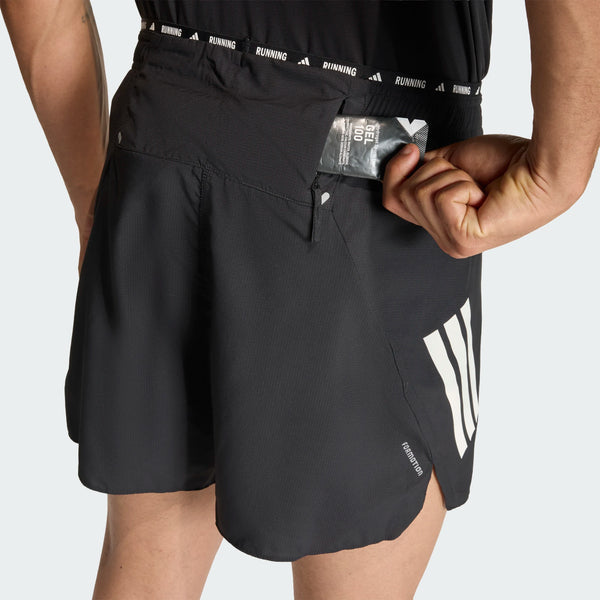 En person stikker en energigel ned i baglommen med lynlås på sorte Adidas Adi365 Shorts, Herre, som har et "RUNNING"-mærke i linningen og et lodret print på venstre ben.